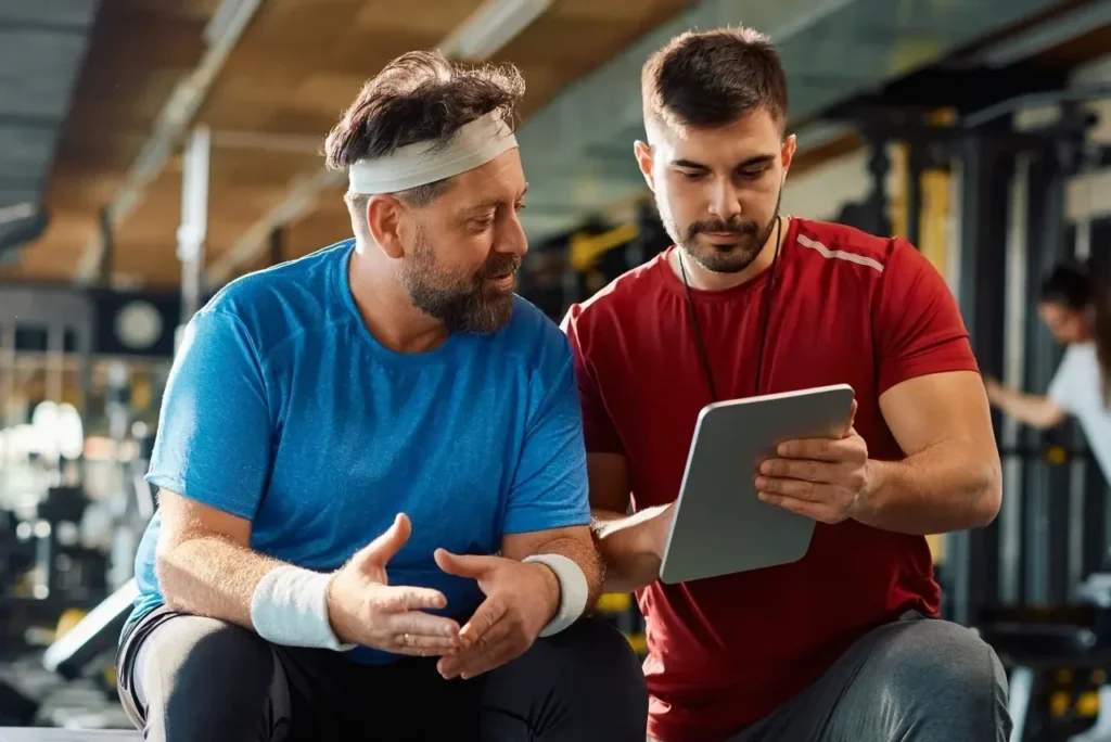 Two men discussing workout plan in gym.
