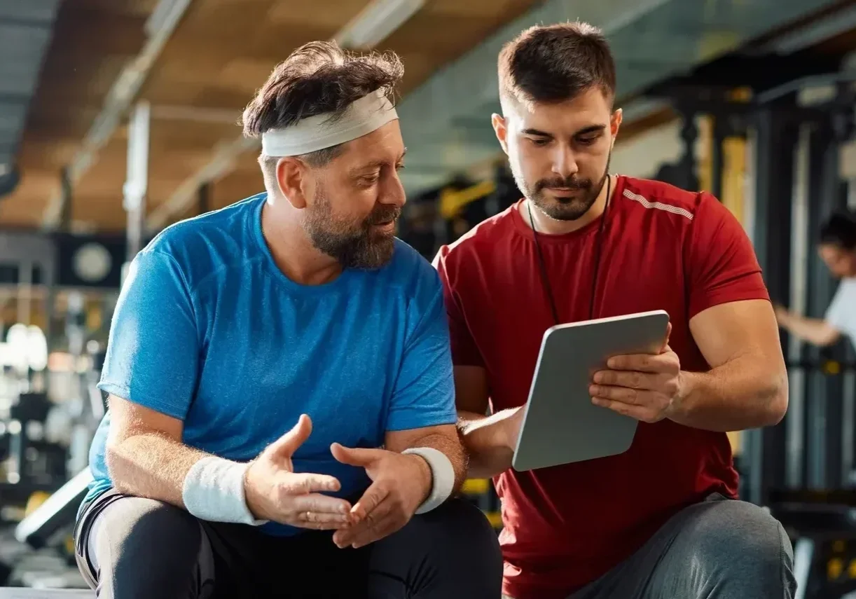 Two men discussing workout plan in gym.